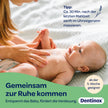 Frau cremt Bauch von Baby auf Decke ein, Text und farbige Welle im Vordergrund