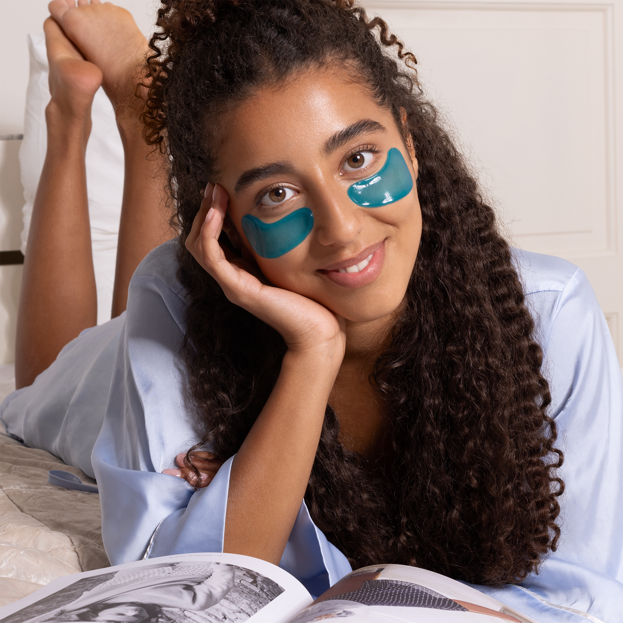 Frau mit YEAUTY Eye Pad Mask Deep Hydration liegend auf dem Bett mit Zeitschrift