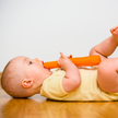 Liegendes Baby auf dem Rücken liegend mit Möhre in Hand und Mund