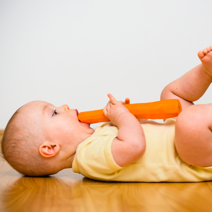 Liegendes Baby auf dem Rücken liegend mit Möhre in Hand und Mund