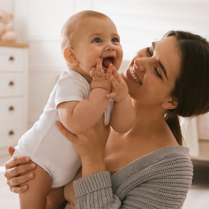 Frau mit Kind auf dem Arm im Kinderzimmer, Kind greift sich in den Mund