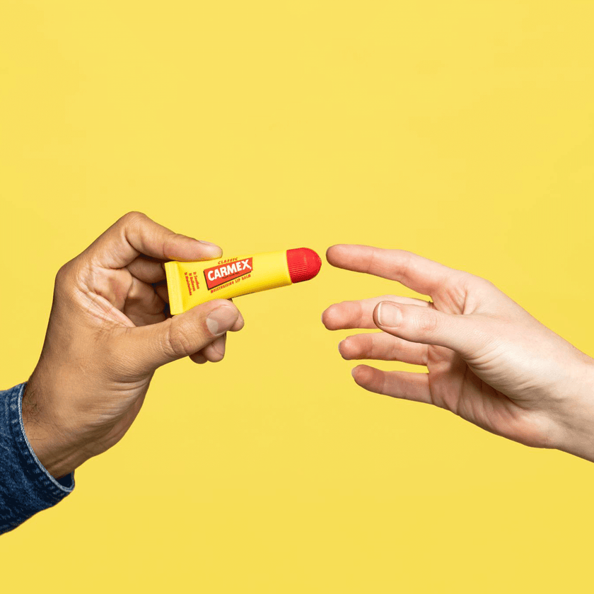 Eine Hand übergibt die Carmex Classic Tube in eine andere Hand