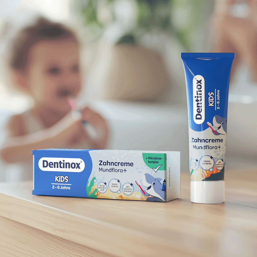 Kind unscharf im Hintergrund Zähne putzend und auf dem Tisch Tube und Verpackung im Vordergrund