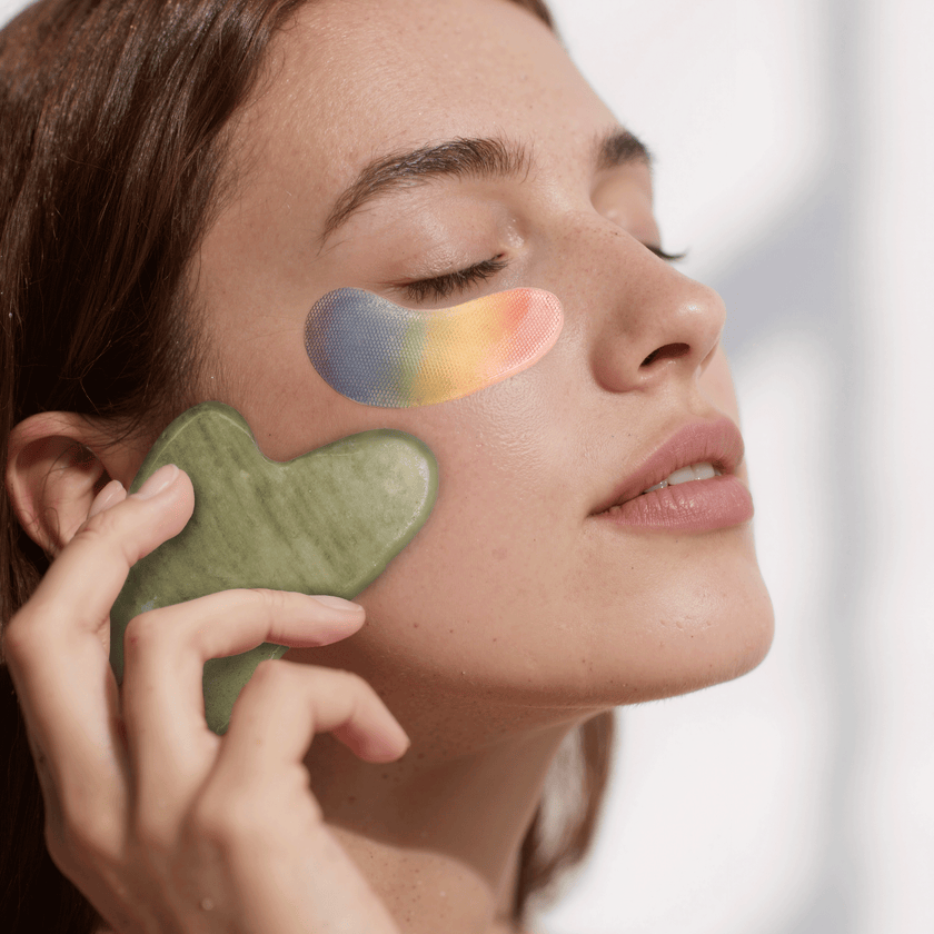 Frau mit Gua Sha Stein an der Wange und YEAUTY Eye Pad Mask Extreme Energy unter den Augen